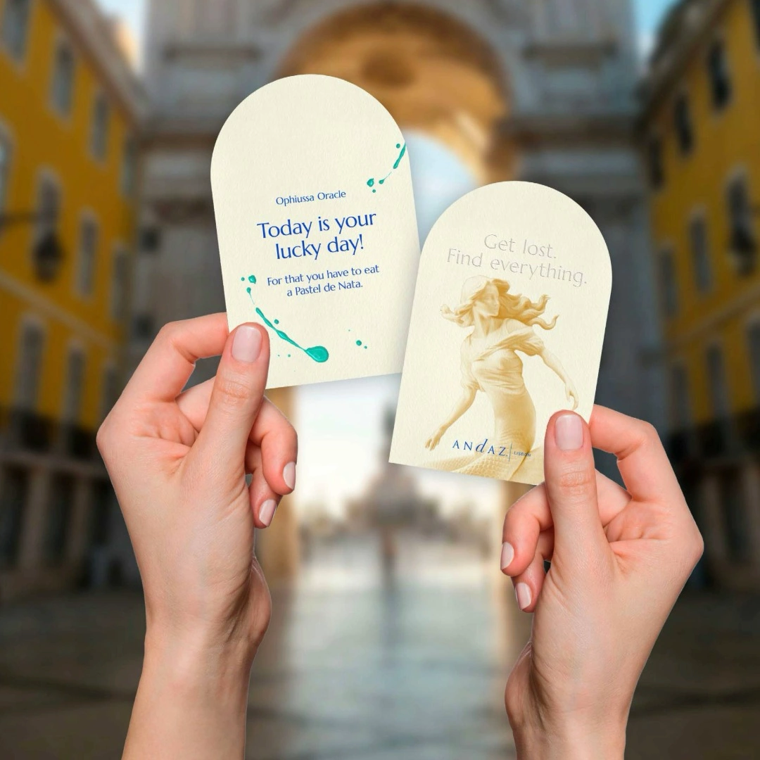 Two hands holding Andaz Lisbon oracle cards with inspirational travel messages against a Lisbon city backdrop
