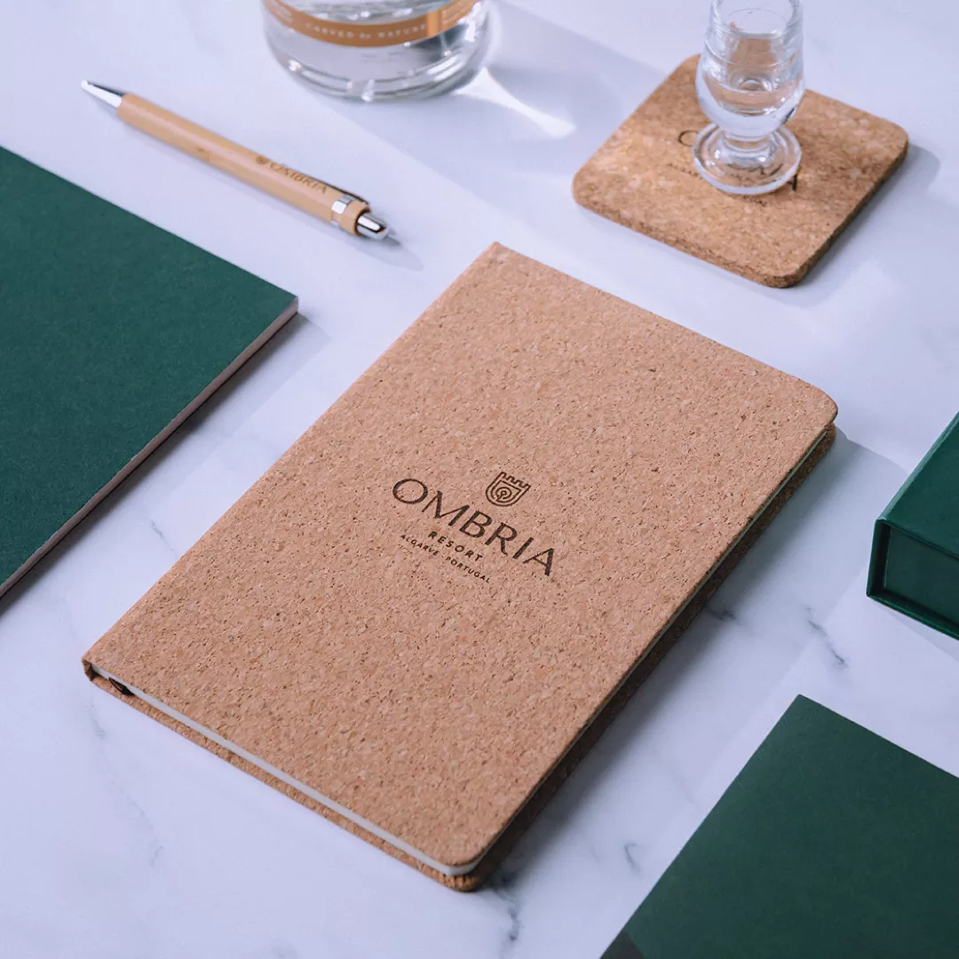 Cork notebook with Ombria brand identity on marble desk with pen, coaster, and green folders