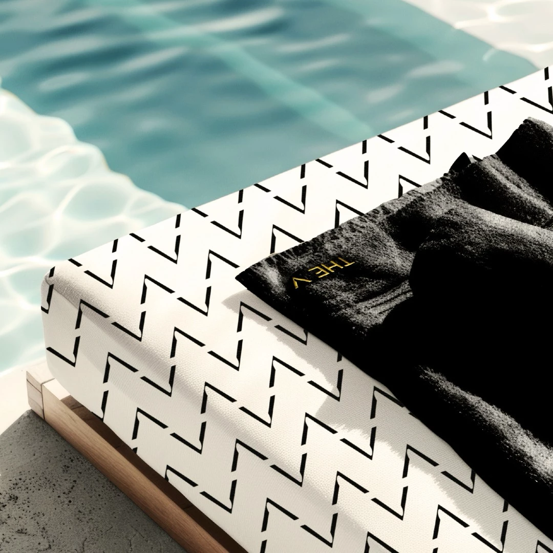 Poolside lounge chair with black and white patterned fabric and black towel featuring TheV Apartments logo