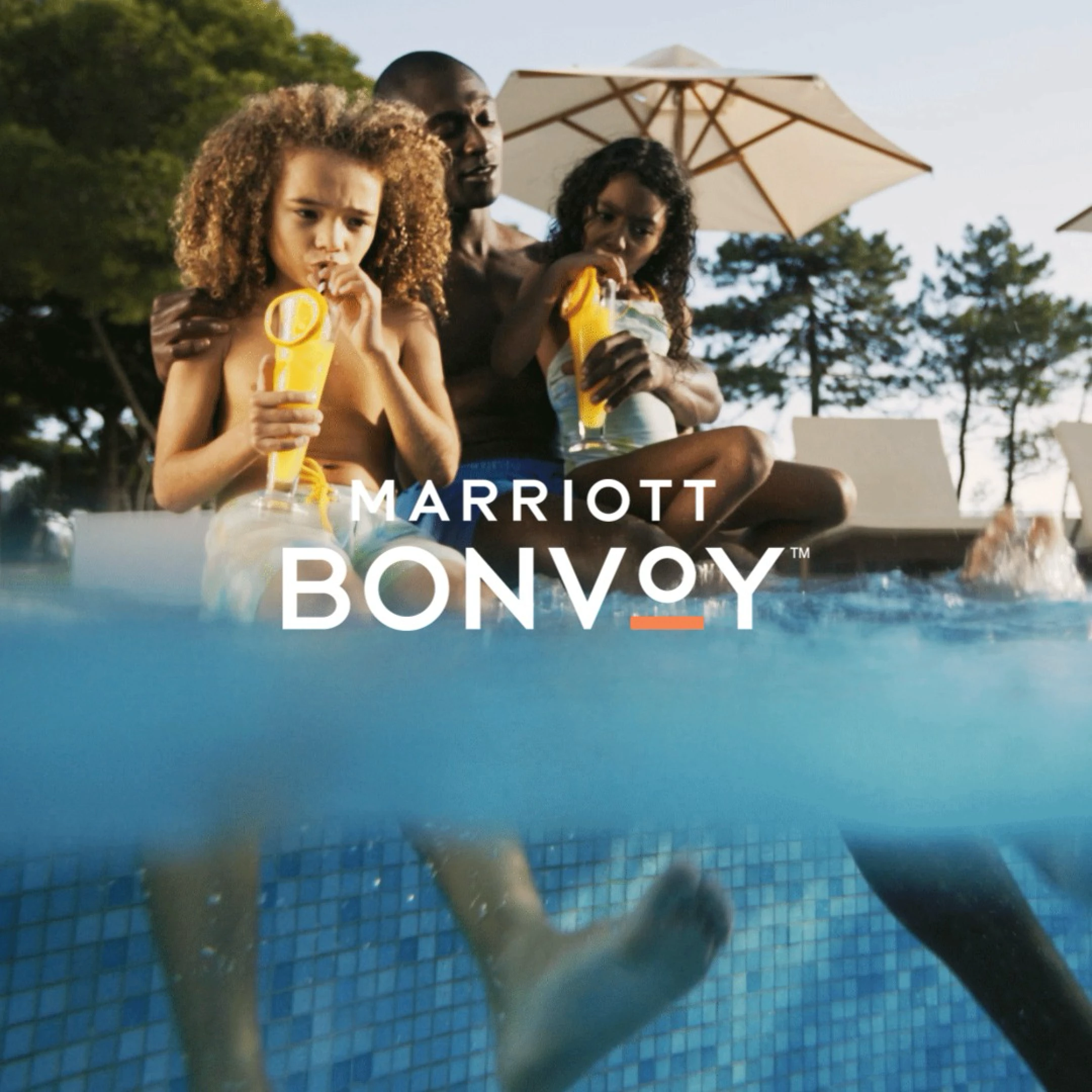 Family sitting by a pool drinking orange juice with Marriott Bonvoy logo overlay