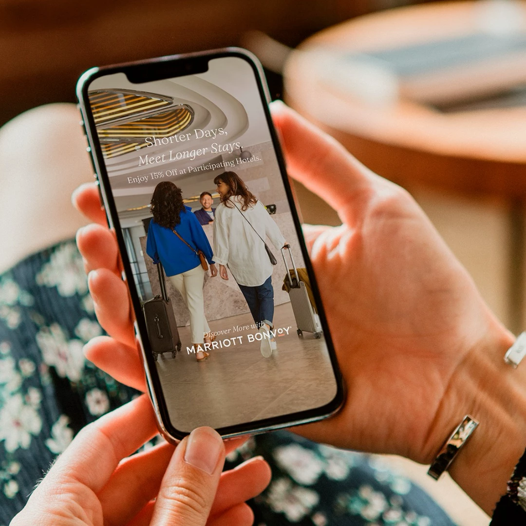 Two friends walking through a hotel lobby shown on smartphone screen with Marriott Bonvoy offer