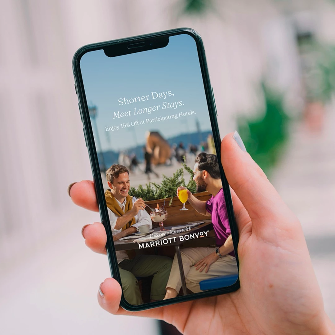 Two friends sharing drinks outdoors with Marriott Bonvoy hotel offer displayed on smartphone screen